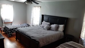 Un dormitorio con una cama grande, dos camas más pequeñas, suelo de madera, un ventilador de techo y cortinas.