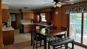 Una cocina con armarios de madera, una mesa de comedor con sillas, un ventilador de techo y vistas a un balcón con mobiliario exterior.