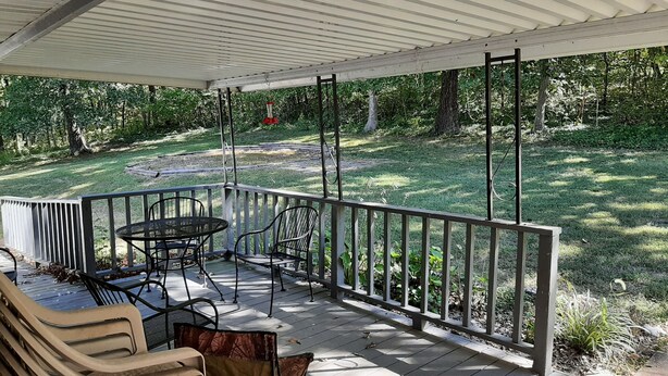 Un patio cubierto con mesa y sillas, una parrilla y vista a un jardín con césped.