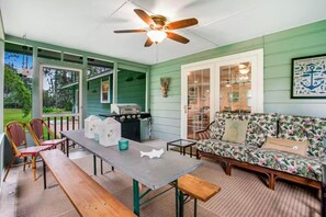 Une véranda abritée comprenant une table à manger, des chaises, un barbecue et un canapé recouvert d’un tissu à motifs floraux.
