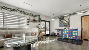 A modern lobby with a seating area, a glass-top coffee table, a board game table, and a large painting on the wall. - Family staycation suite near Six Flags in The Landing Hub Hotel with onsite activities (Pacific)