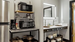 A compact kitchen with a microwave, toaster oven, and coffee maker on a shelf, a refrigerator, and a sink with a mirror above. - Family staycation suite near Six Flags in The Landing Hub Hotel with onsite activities (Pacific)