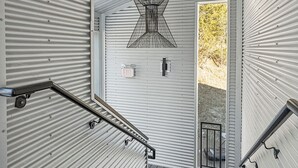 Eine Treppe mit Metallgeländern, eine Decke mit einer geometrischen Leuchte und eine Tür mit der Aufschrift 'EXIT'.