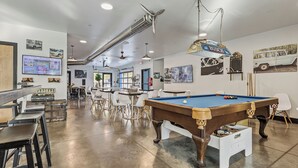 Ein Billardraum mit Pooltisch, Stühlen und einem Fernseher, der ein Spiel zeigt.