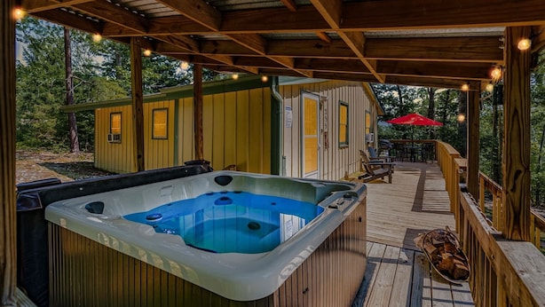 Une terrasse en bois avec un jacuzzi, des sièges d’extérieur et un petit bâtiment doté d’une porte et de fenêtres.