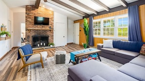 Un salon avec une cheminée, un ventilateur de plafond, un canapé et une grande fenêtre avec des rideaux.