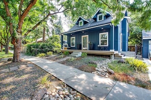A two-story house with a dark blue exterior, a front porch with steps, and a garden with rocks and plants.