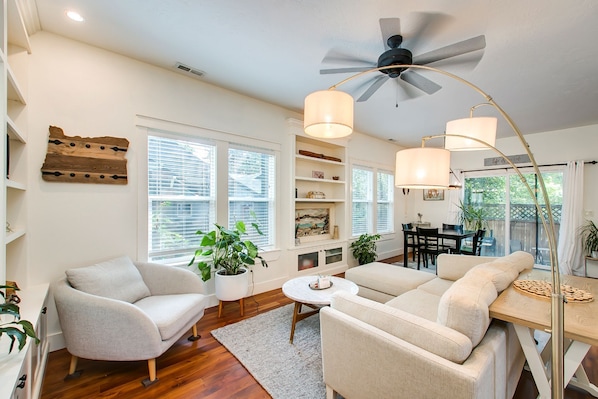 A spacious living room with a ceiling fan, two sofas, a dining table, and a kitchen area visible through an open door.