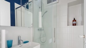 A modern bathroom with a glass-enclosed shower, a white sink, and a blue glass.