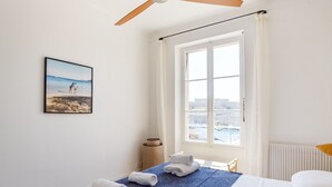 A hotel room with a bed, a window with a view of the city, a ceiling fan, and a framed picture on the wall.