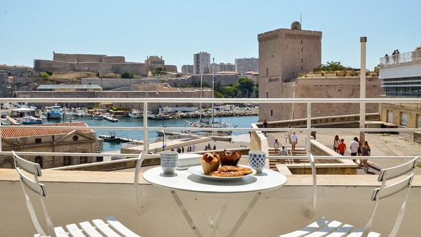 A balcony with a table set for two, overlooking a marina with boats and a historic fort.
