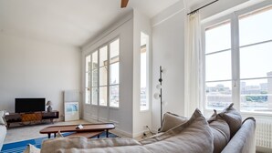 A modern living room with a large window, a sofa, a coffee table, a TV, and a radiator.