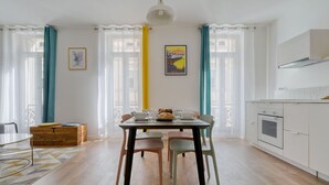 Moderni keittiö, jossa on valkoiset kaapit, sisäänrakennettu uuni ja ruokailutila, jossa on neljälle katettu ruokapöytä.