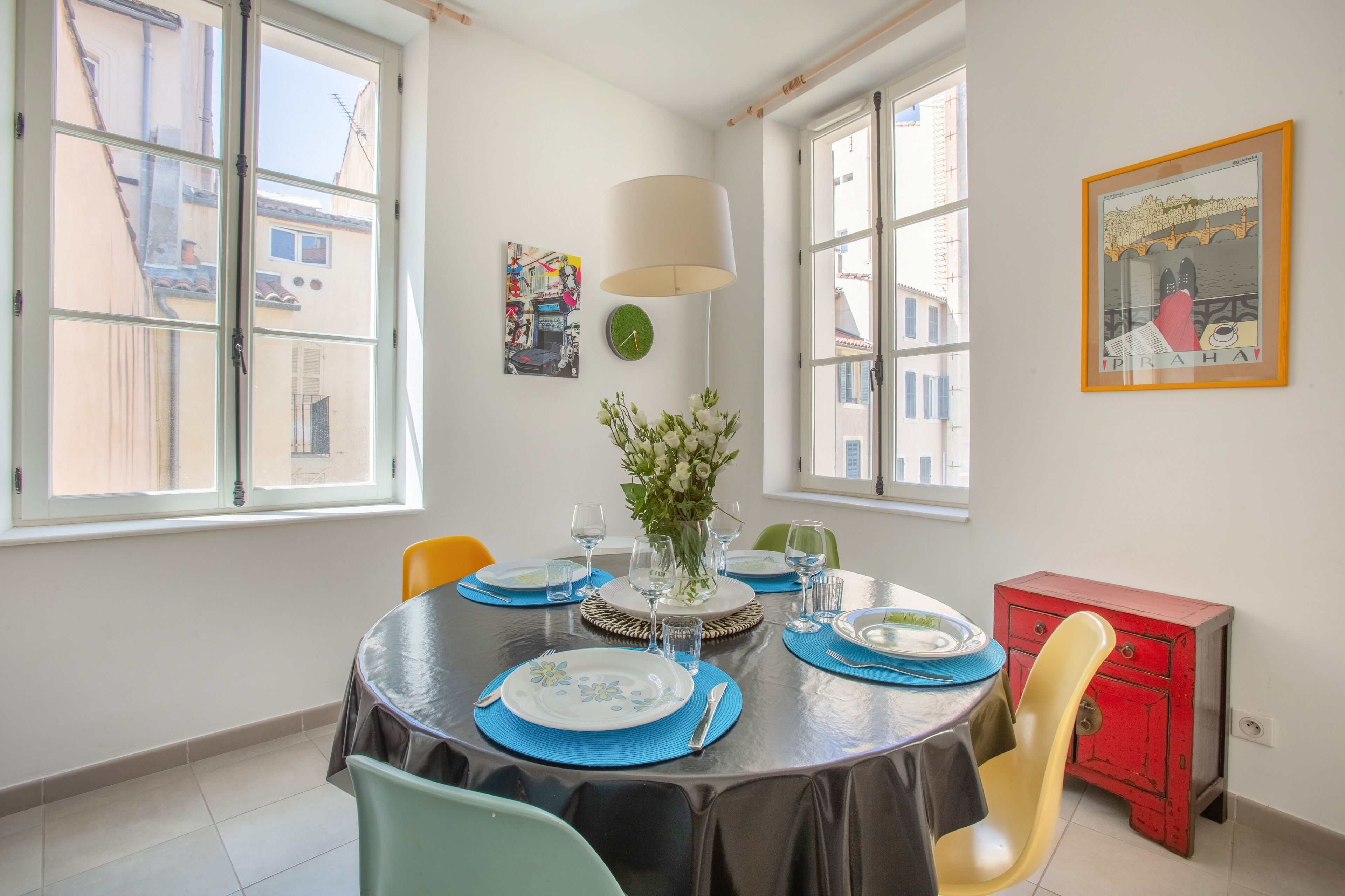A dining area with a round table set for four, a vase of flowers, and a red cabinet.