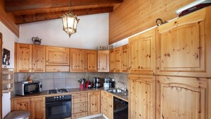 A kitchen with wooden cabinets, a stove, a microwave, a sink, and a dishwasher. - Chalet Anne Sophie (Riddes)