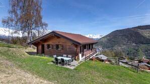 A wooden cabin with a sloped roof, a patio with outdoor seating, and a view of snow-capped mountains in the background. - Chalet Anne Sophie (Riddes)