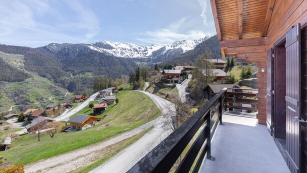 A mountain village with wooden houses, a winding road, and snow-capped peaks in the background. - Chalet Anne Sophie (Riddes)
