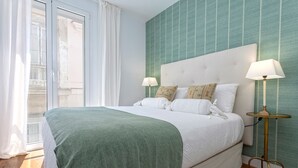 A bedroom with a large bed, two bedside lamps, a green throw blanket, and a view of a building through a window. - Genteel Home San Antonio IV (Cadiz)