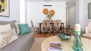 A living room with a sofa, coffee table, and a magazine. There is a dining area with a table and chairs. - Genteel Home San Antonio IV (Cadiz)
