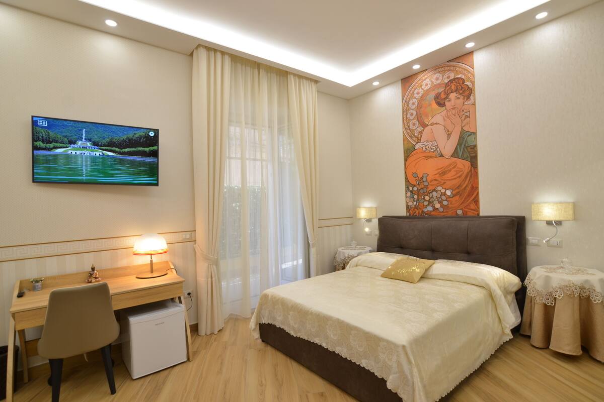 A hotel room with a bed, desk, chair, and a TV on the wall.