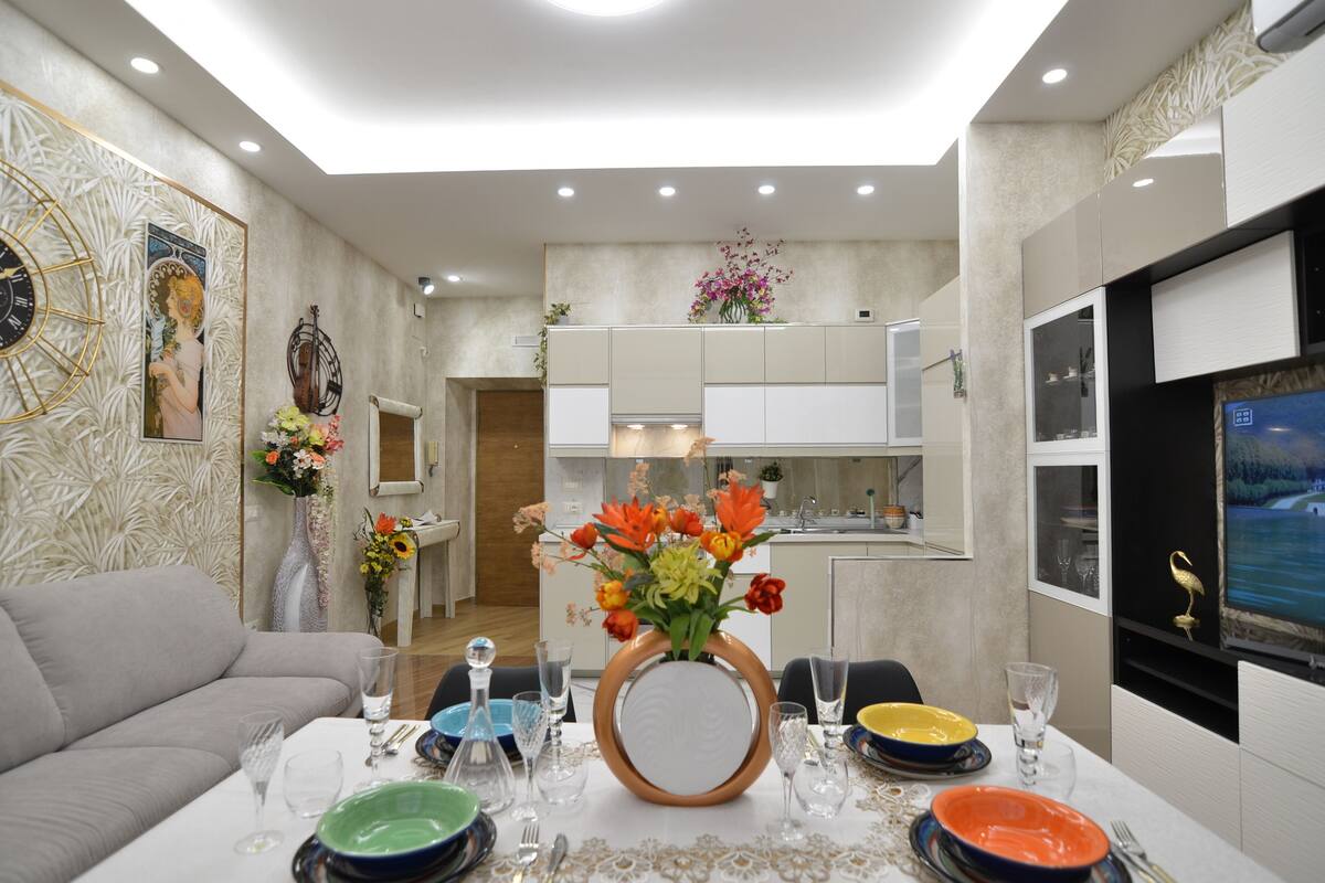 A modern dining area with a table set for four, a sofa, and a kitchen in the background.