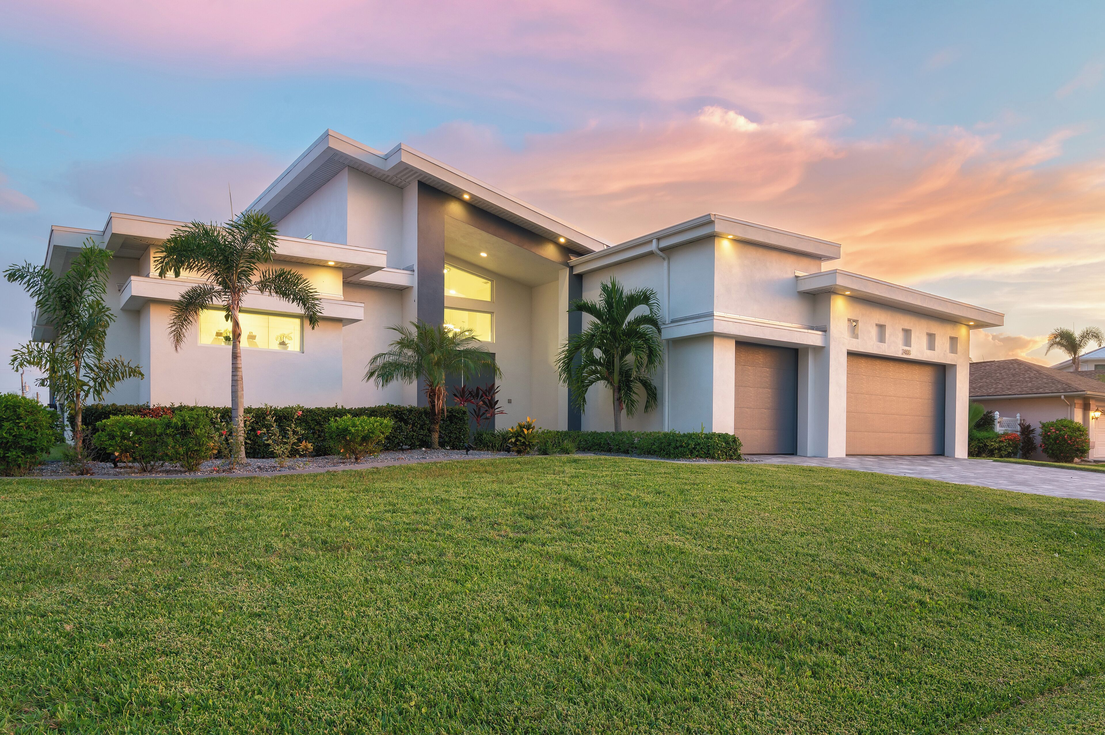 A modern two-story house with a well-maintained lawn, palm trees, and a garage.