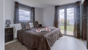 A bedroom with a large bed, a bedside table, a lamp, and a view through the glass door. - Villa Atalaya (Peñíscola)