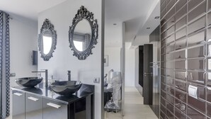 A modern bathroom with two large oval mirrors, a black sink with a bowl, and a glass-tiled wall. - Villa Atalaya (Peñíscola)