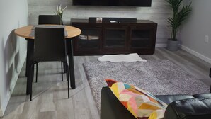 Ein modernes Wohnzimmer mit Flachbildfernseher an der Wand, einem Esstisch mit Stühlen, einer Couch und einer großen Topfpflanze.
