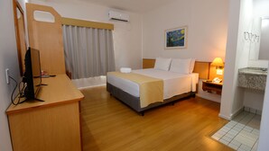 Habitación de hotel con una cama, un escritorio con computadora, una lámpara de noche y un cuadro en la pared.