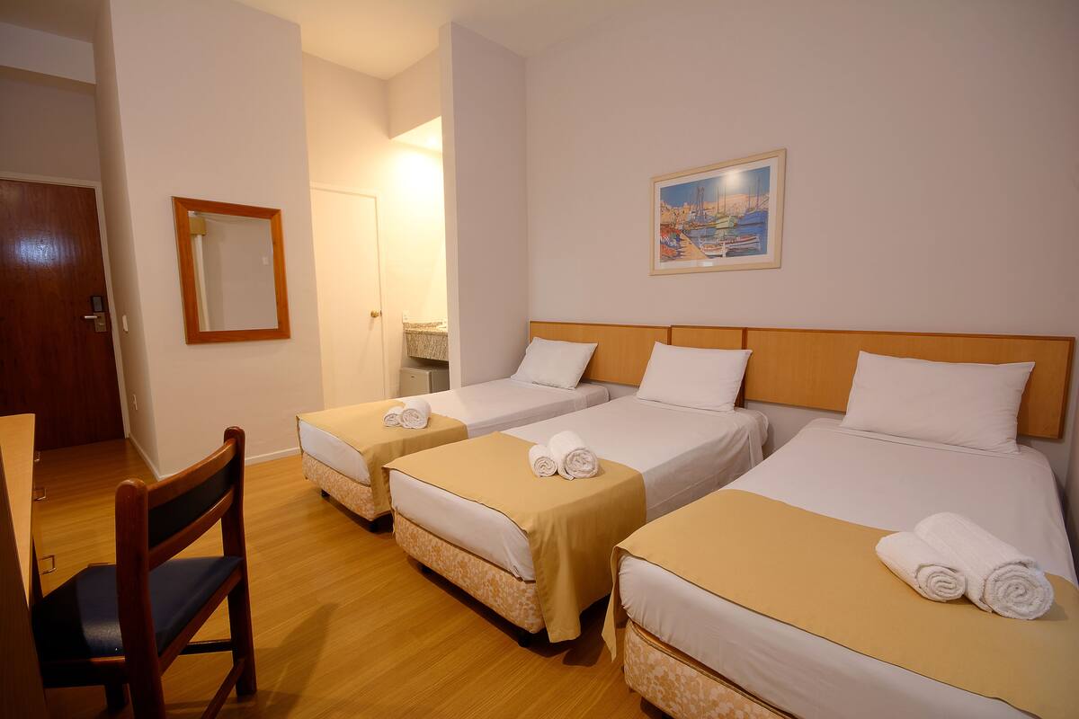 Hotellihuone, jossa on kaksi erillistä sänkyä, puinen tuoli ja taulu seinällä.
