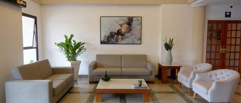 A modern living room with a sofa, two armchairs, a coffee table, and a painting on the wall.