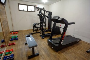 Une salle de sport équipée d’un tapis de course, d’un banc de musculation et de différents haltères.