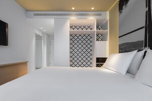 A modern hotel room with a large bed, built-in wardrobe, and a cityscape view.