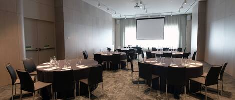 Un salón de conferencias con varias mesas redondas, cada una con sillas y vasos de agua.