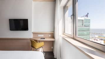 Habitación de hotel con cama, escritorio, silla, televisor y ventana con vista a la ciudad.