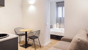 A compact living space with a kitchenette, a dining area with two chairs, a bed, and a sofa. - Apartamentos Líbere Valencia Jardín Botánico (Valencia)