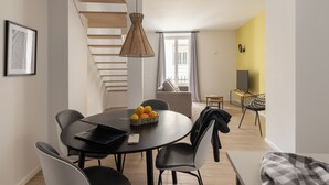 A modern dining area with a round table, black chairs, and a basket of oranges. A staircase with wooden steps leads to a balcony. - Apartamentos Líbere Valencia Jardín Botánico (Valencia)