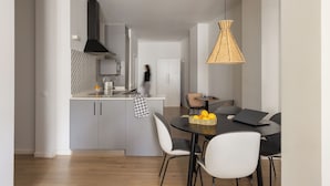 A modern kitchen with grey cabinets, a black range hood, and a dining area with a round table and chairs. - Apartamentos Líbere Valencia Jardín Botánico (Valencia)