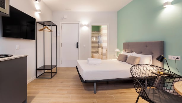 A modern hotel room with a bed, a desk, a chair, and a TV. - Apartamentos Líbere Valencia Jardín Botánico (Valencia)