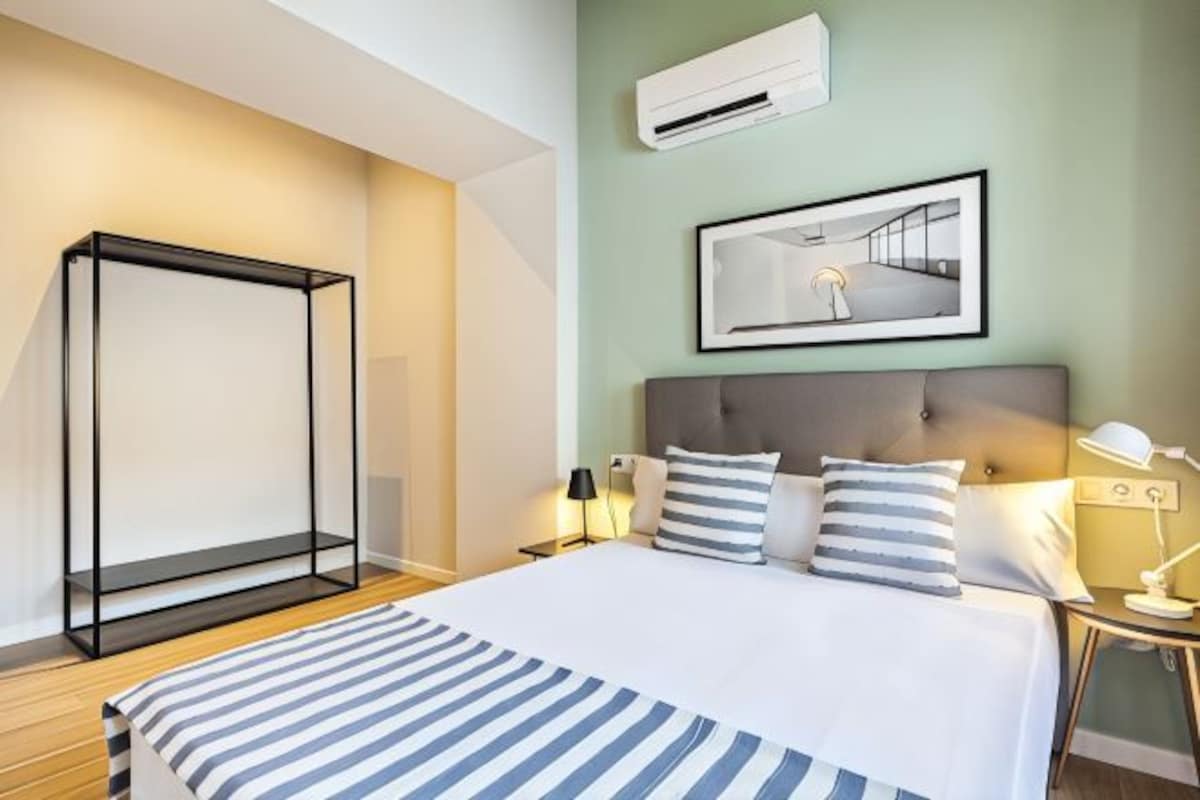 Una habitación de hotel con una cama, mesitas de noche, una lámpara de pie y un cuadro en la pared.
