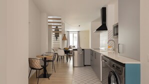 A modern kitchen with a washing machine, a dining area with a table and chairs, and a staircase leading to another level. - Apartamentos Líbere Valencia Jardín Botánico (Valencia)
