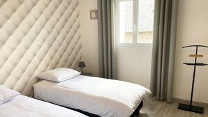 Ein Hotelzimmer mit zwei Betten, einem Fenster mit Vorhängen, einem Nachttisch mit Lampe und einer Stehlampe.