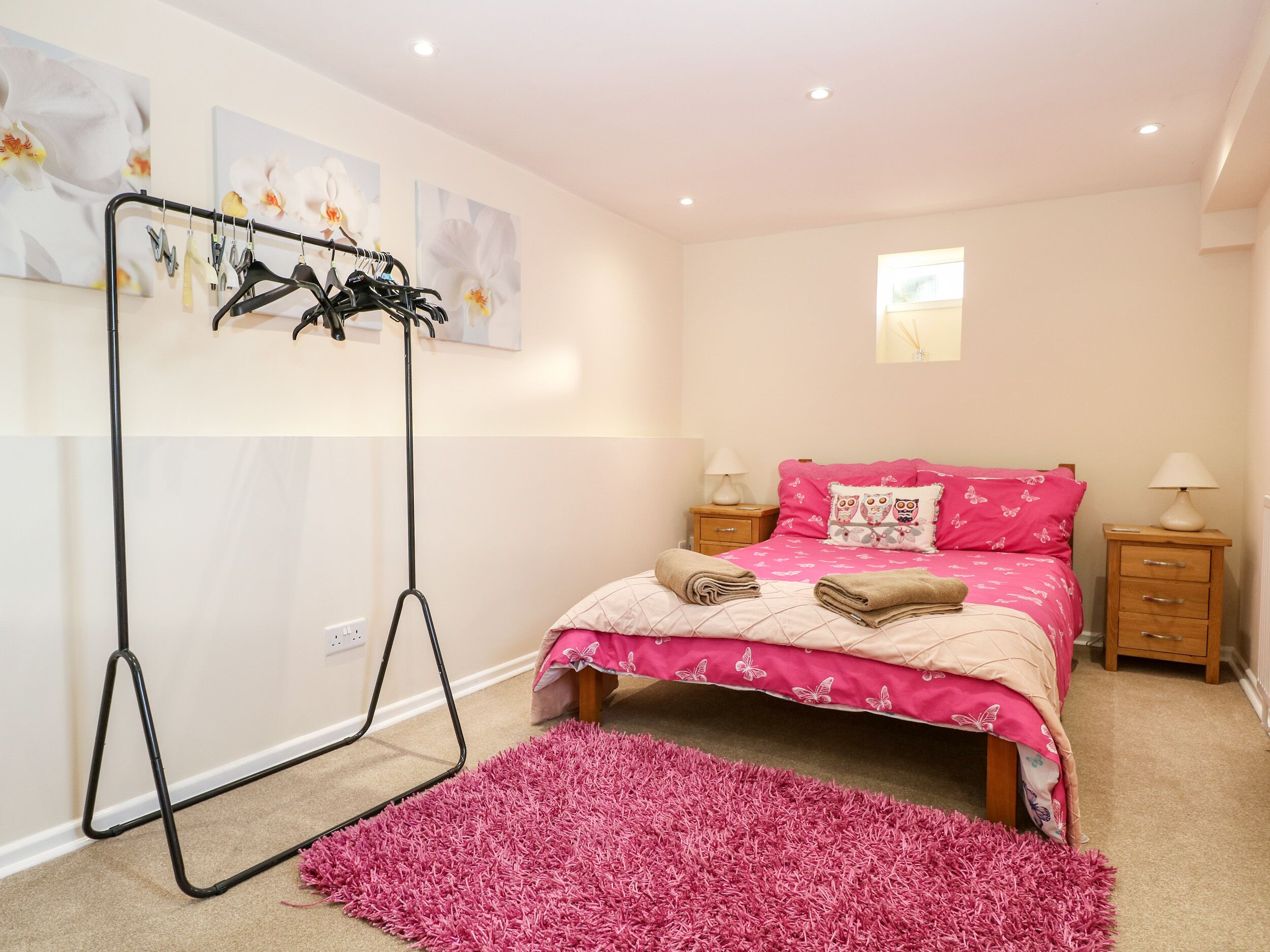 Une chambre avec un lit, deux tables de chevet, un portant à vêtements et un tapis rose.