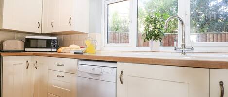 A modern kitchen with white cabinets, a microwave, a toaster, and a dishwasher. There is a window with a view of greenery outside.