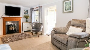 A living room with a fireplace, a television mounted on the wall, a sofa, a chair, and a rug. - Cosy Cottage (Bexhill-on-Sea)