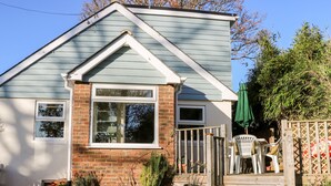 A house with a gabled roof, a front porch with a wooden railing, and a brick facade. - Cosy Cottage (Bexhill-on-Sea)