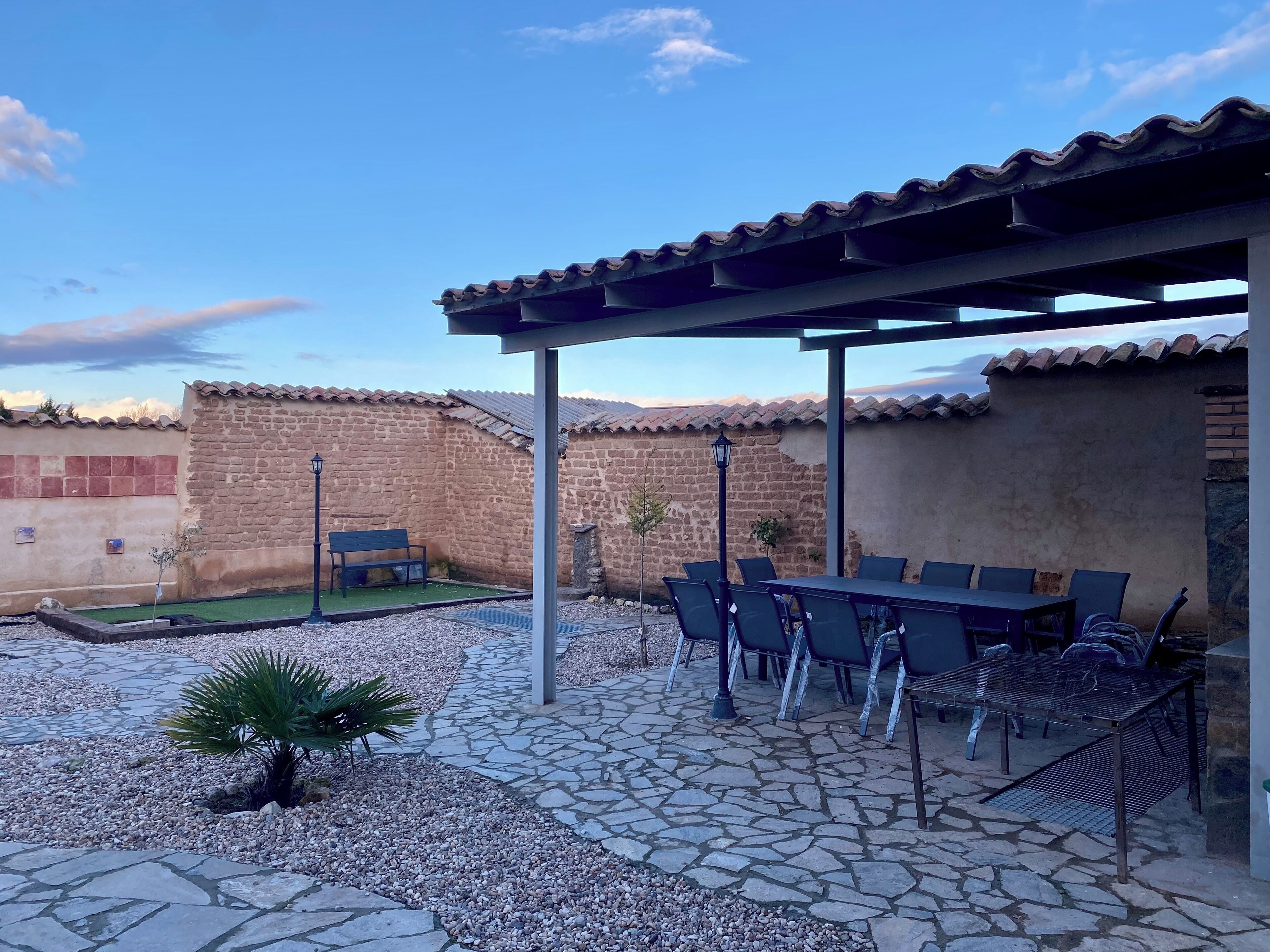 Une terrasse avec un sol en pierre, une table entourée de chaises, une pergola et un mur en pierre.