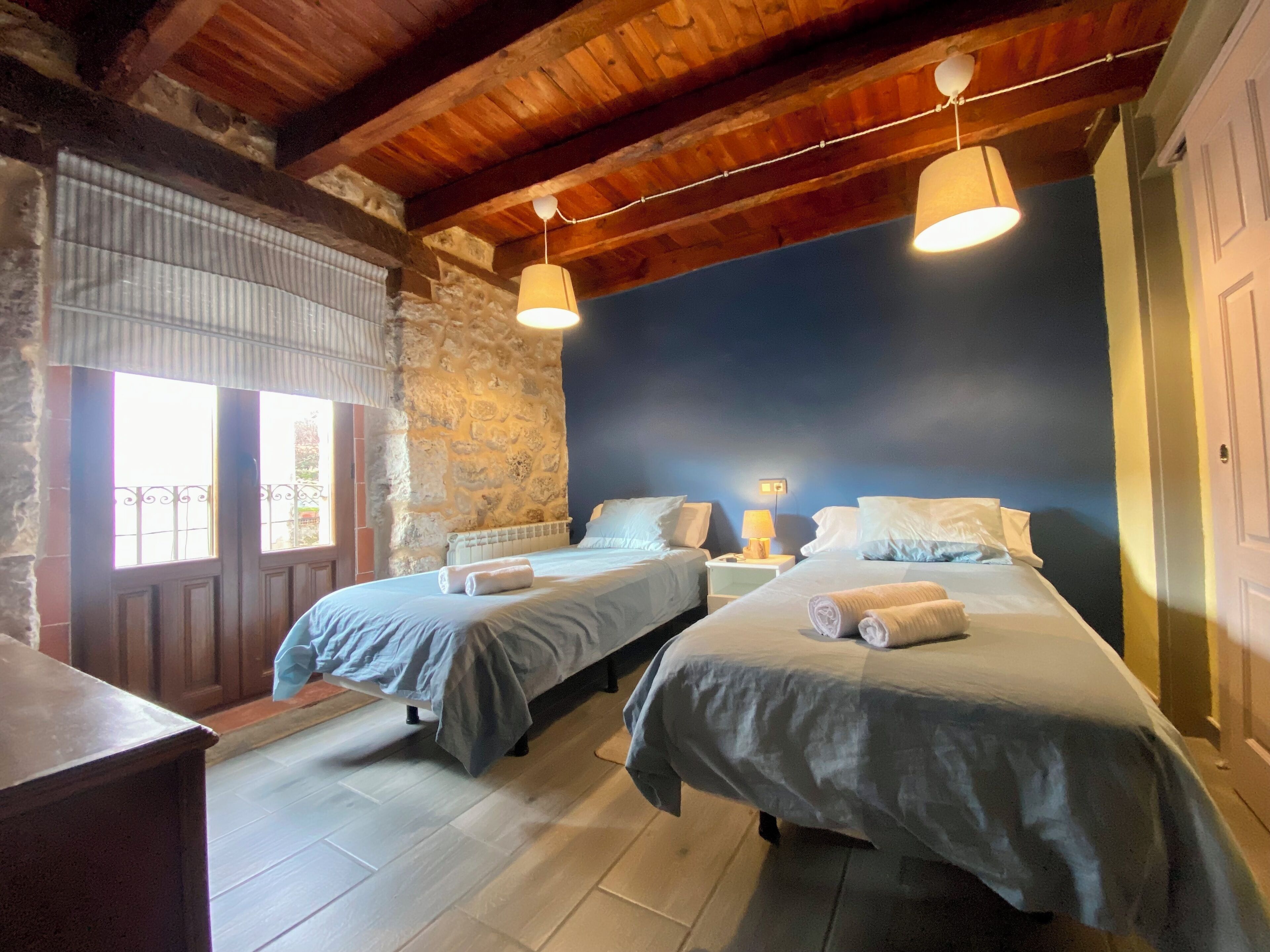 Una habitación con dos camas, vigas de madera, paredes de piedra y una ventana con persianas.