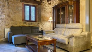 Un salon avec un mur en pierre, un meuble en bois, un canapé gris et un canapé beige.